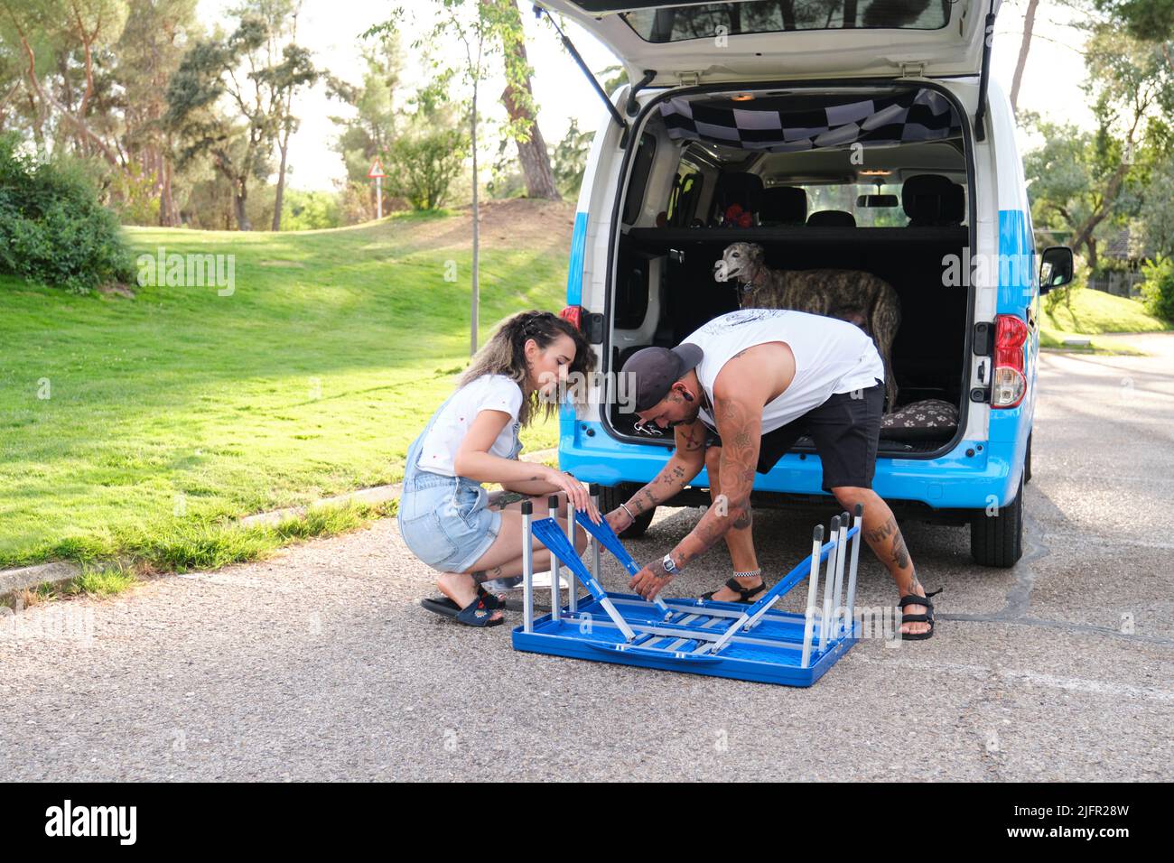 Giovane coppia tatuata montaggio tavolo da picnic pieghevole vicino al furgone. Foto Stock