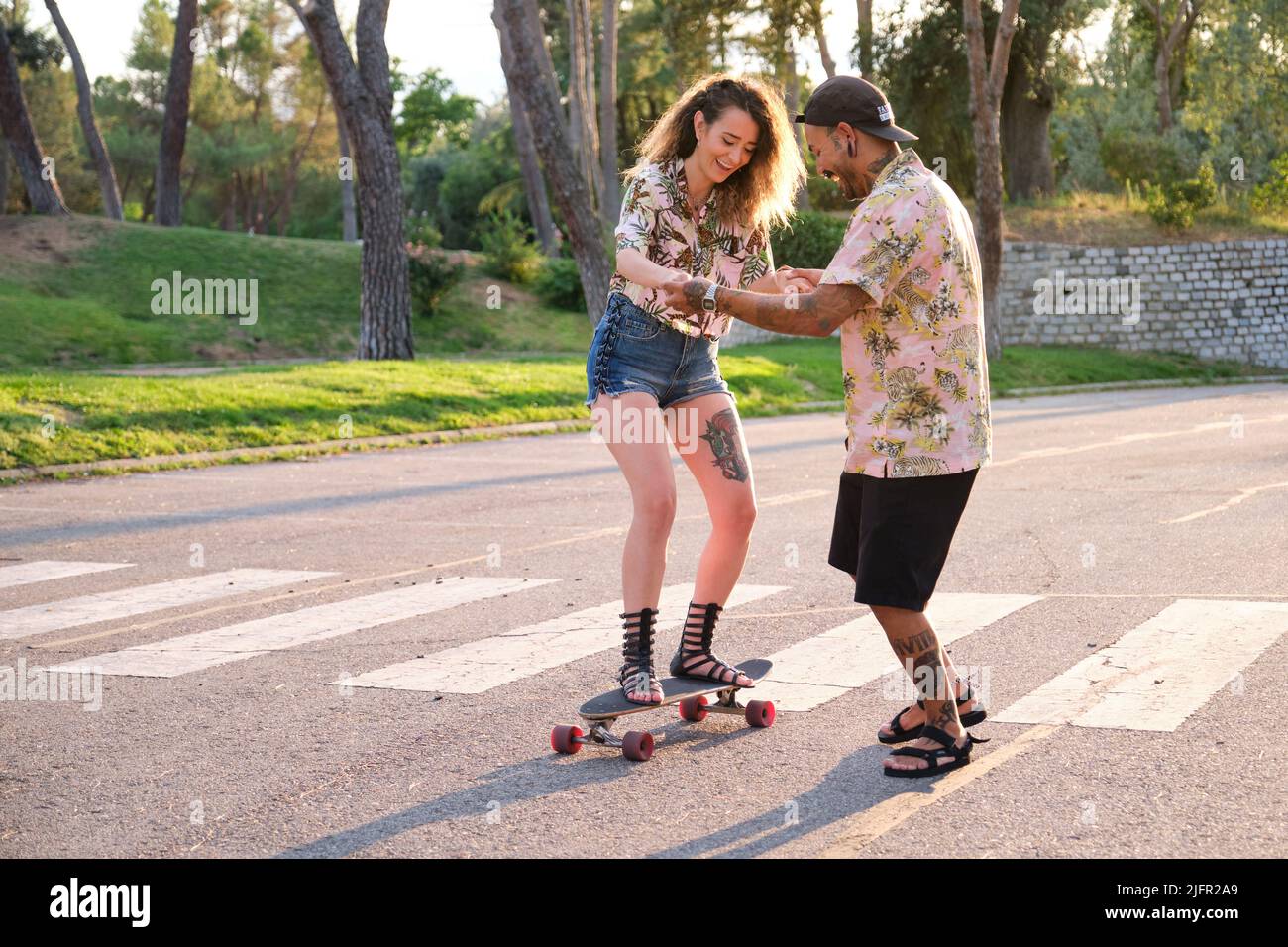Giovane uomo fresco tatuato che insegna alla sua ragazza come skateboard. Foto Stock