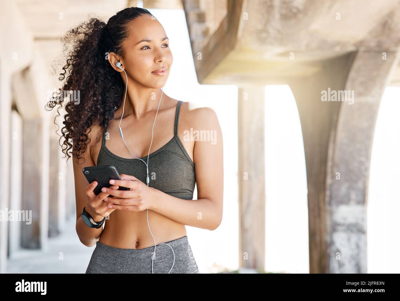 So che posso fare di meglio. Scatto di una giovane donna attraente in piedi in città e utilizzando il suo cellulare per ascoltare la musica durante il suo allenamento. Foto Stock