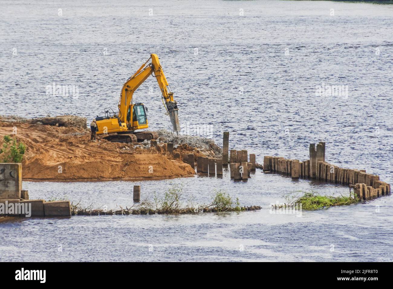Escavatore sulla riva del fiume con un ugello a martello pneumatico, lavoro di miglioramento del terrapieno Foto Stock