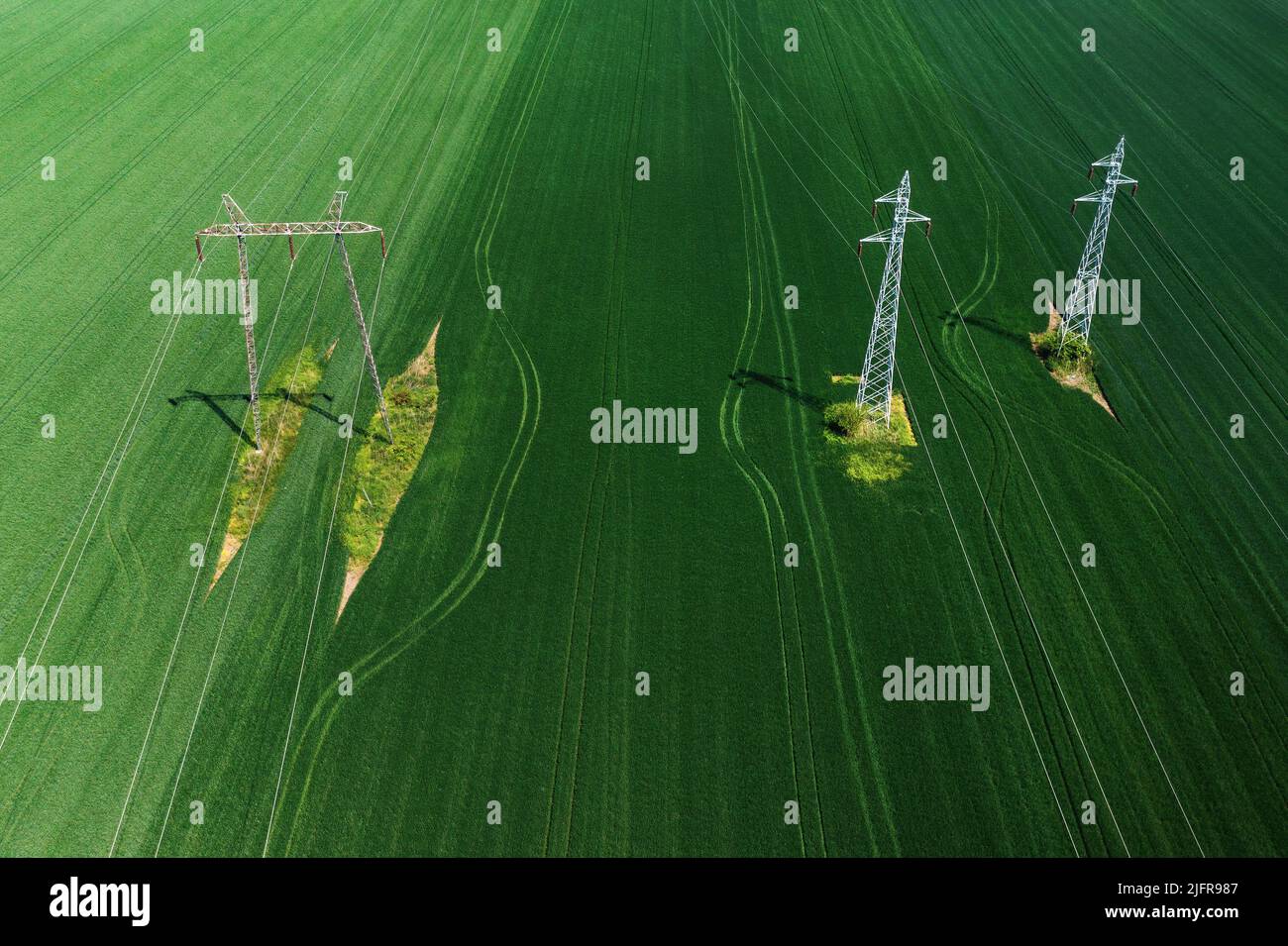 Tiro aereo di piloni elettrici e torri di trasmissione in campo agricolo coltivato dal drone pov Foto Stock