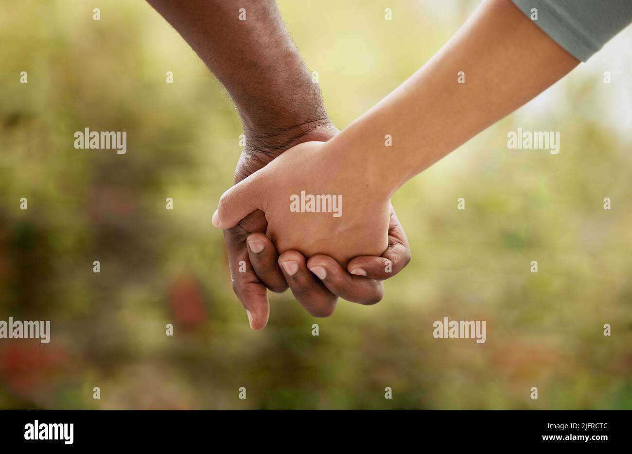 Primo piano della coppia biraciale che interblocca le dita e tiene le mani mentre si legano nel giardino a casa. Razza mista donna unita con africano Foto Stock