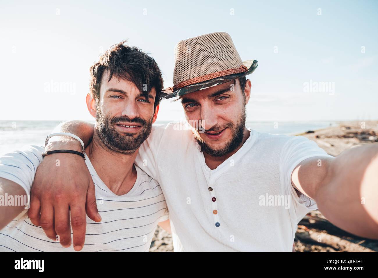 Coppia di giovani ragazzi amici si abbracciano al tramonto sulla spiaggia e si prendono un selfie. Amicizia e concetto di amore Foto Stock