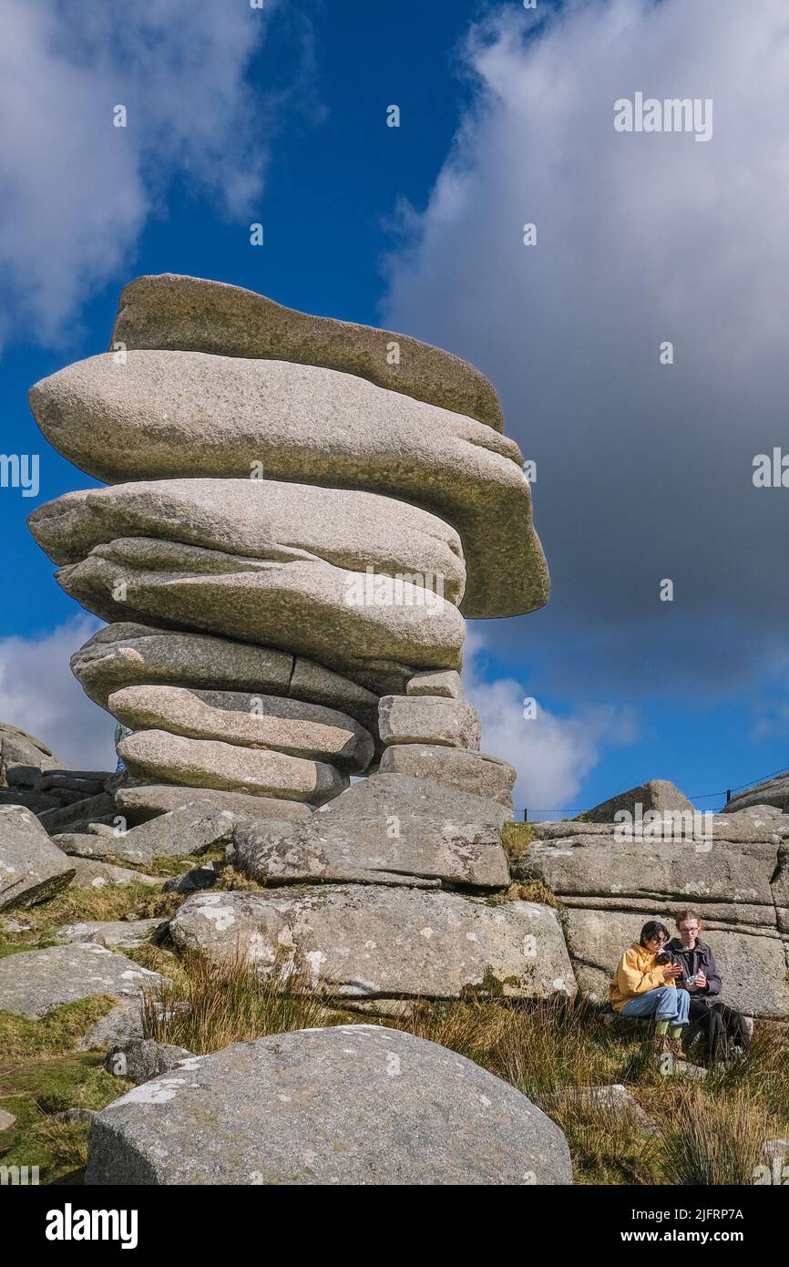 Una giovane coppia che si rilassa sotto la torreggiante roccia di granito, il Cheesewring lasciato dall'azione glaciale su Stowes Hill a Bodmin Moor in Cornovaglia. Foto Stock