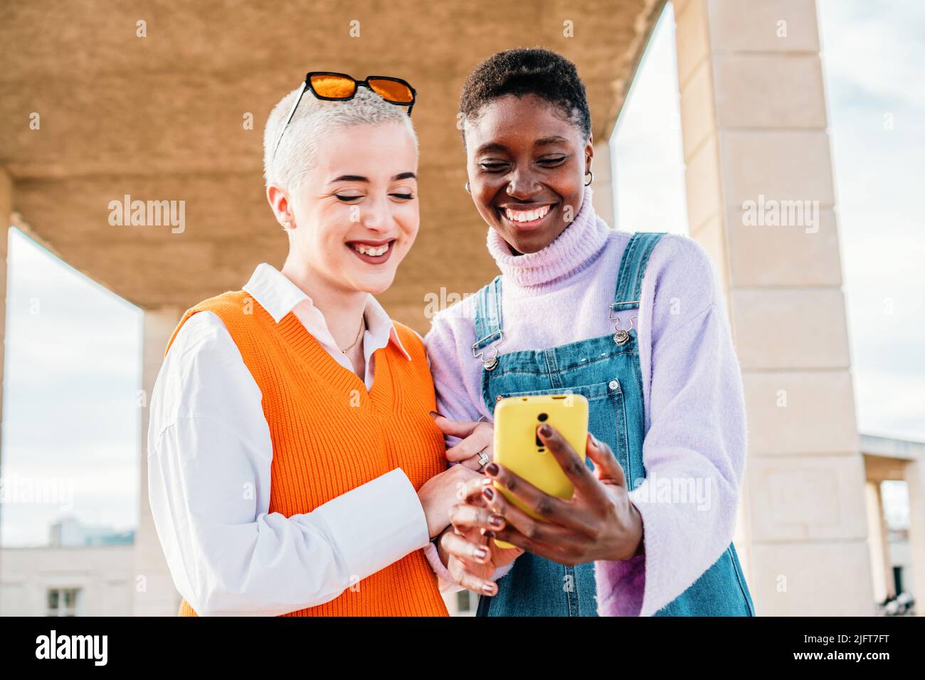 Due amici felici che condividono i file multimediali con uno smartphone insieme. Ragazze multietniche che si divertono con un telefono cellulare all'aperto. Foto Stock