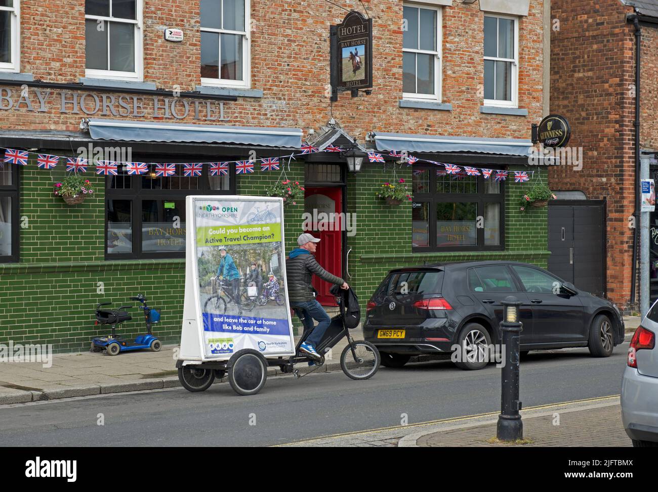Uomo in bicicletta, con segno che promuove i vantaggi di viaggiare in bicicletta, Selby, North Yorkshire, Inghilterra Regno Unito Foto Stock