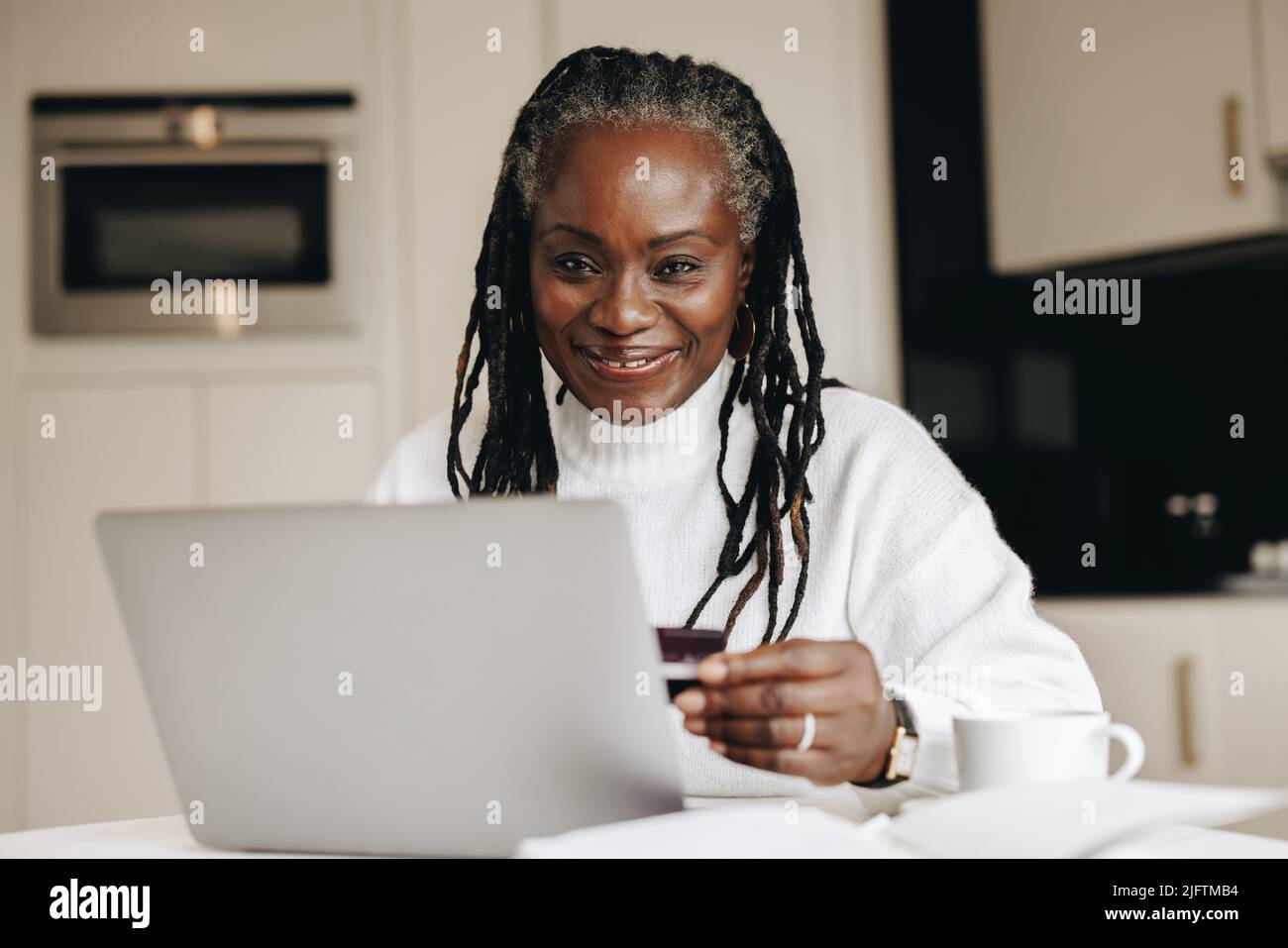 Donna matura felice sorridendo alla macchina fotografica mentre fa un pagamento in linea con una carta di credito. Etnia anziana donna facendo un po 'di shopping online per la sua fre Foto Stock