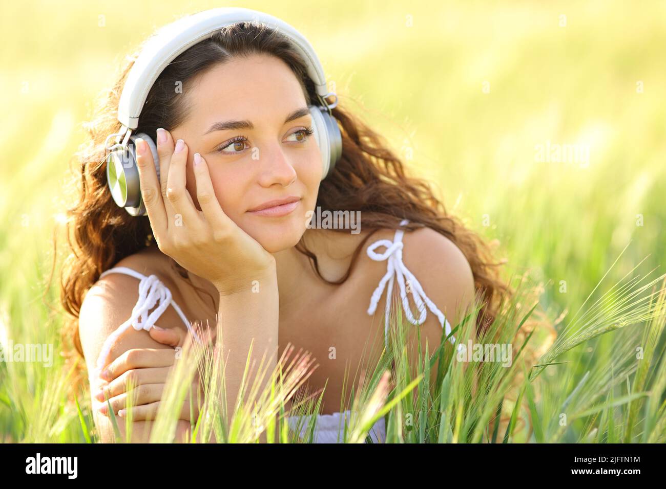 Donna rilassata che indossa le cuffie per ascoltare la musica guardando lateralmente in un campo di grano Foto Stock