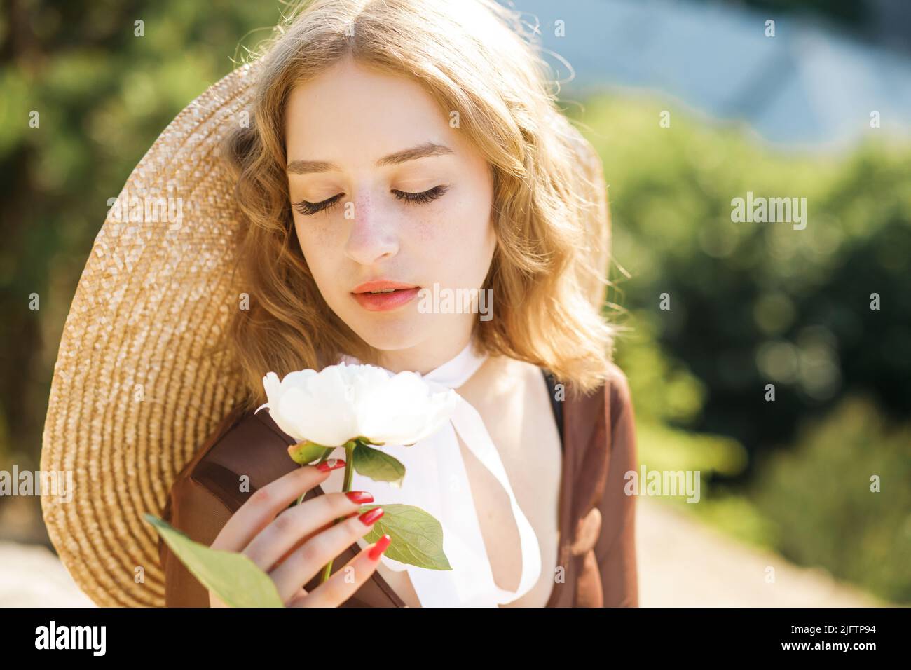 . Una ragazza elegante si pone sullo sfondo della città con un fiore di peonia in mano. Foto Stock