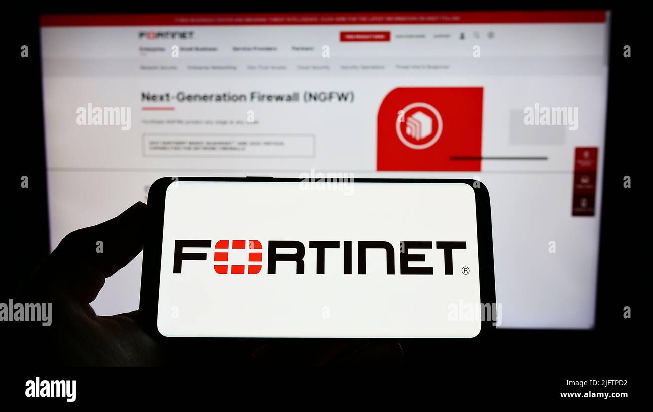 Persona che detiene il telefono cellulare con il logo della società americana di sicurezza informatica Fortinet Inc. Sullo schermo di fronte alla pagina web. Mettere a fuoco sul display del telefono. Foto Stock