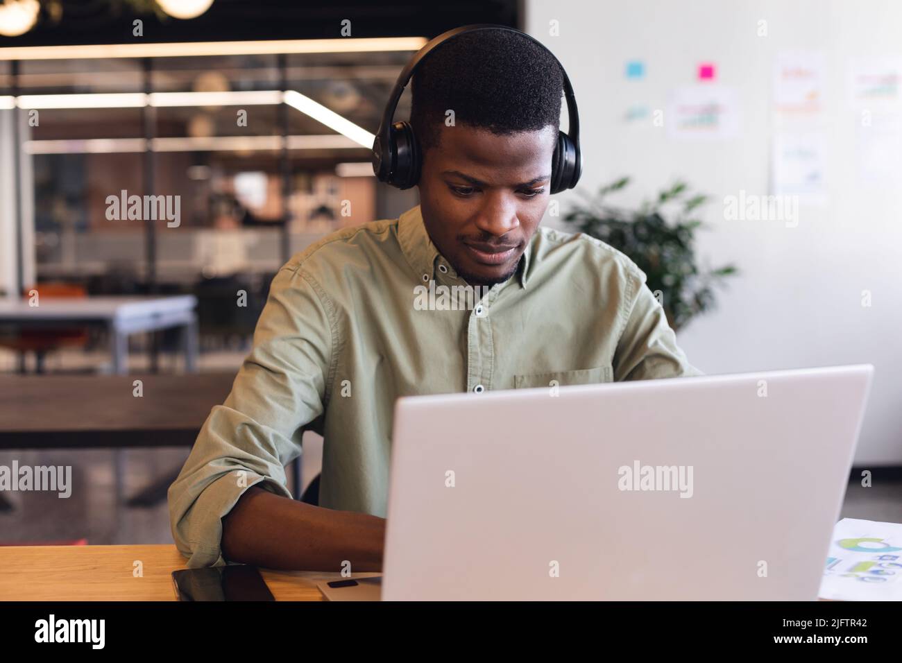 Giovane uomo d'affari afroamericano che indossa cuffie utilizzando un computer portatile in ufficio Foto Stock