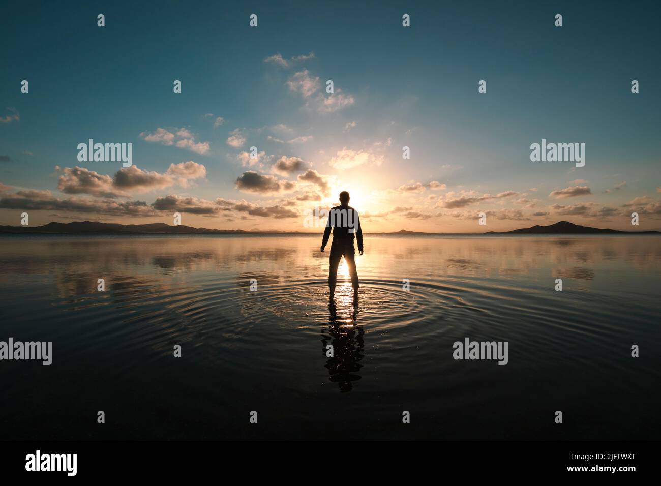 Silhouette di un uomo in piedi con la schiena rivolta al tramonto sulle acque poco profonde del Mar Menor, regione di Murcia, Spagna, creando increspature sul Foto Stock