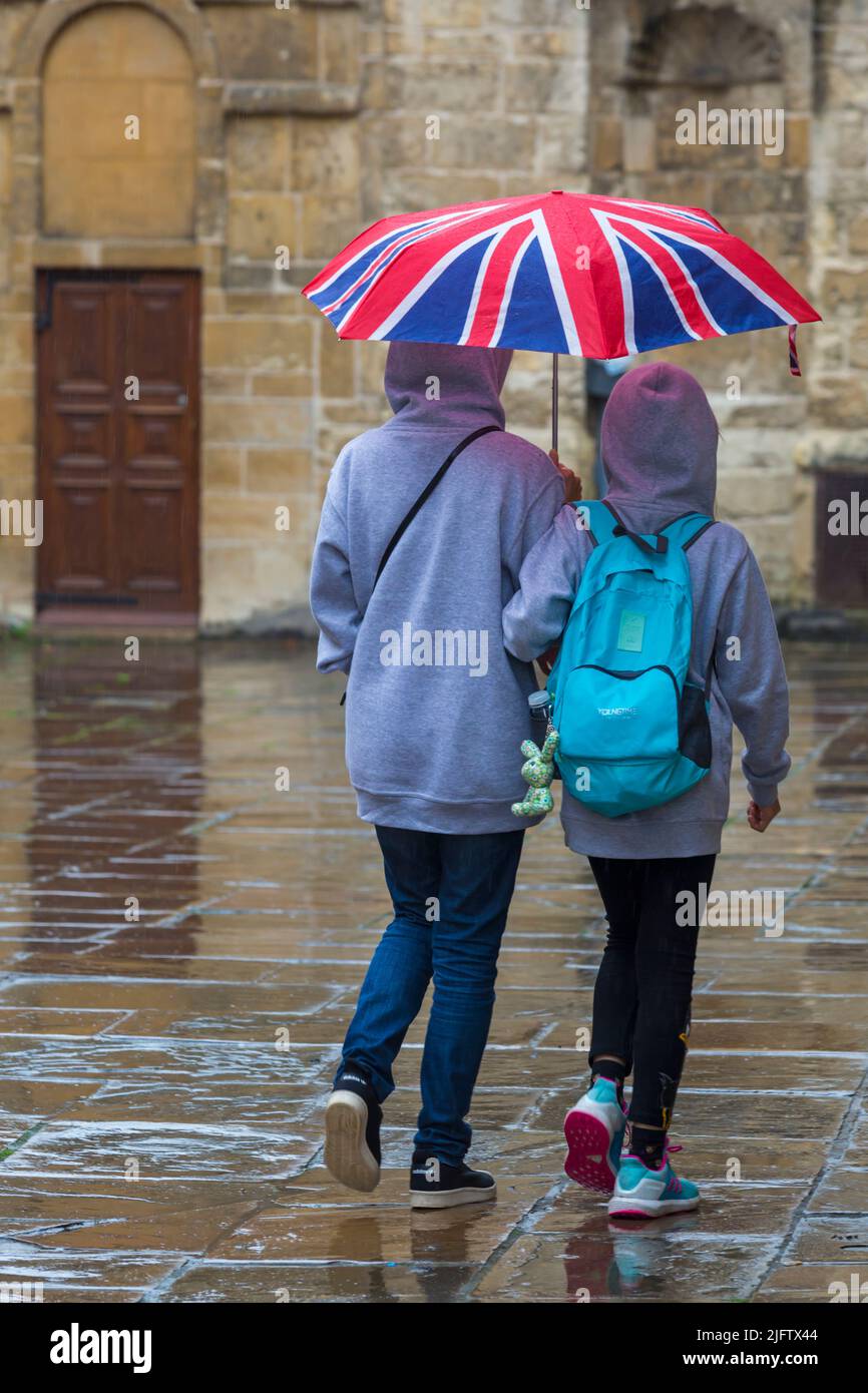 I turisti camminano mentre si riparano sotto l'ombrello di Union Jack nella pioggia battente a Oxford, Oxfordshire Regno Unito in una giornata piovosa bagnata in agosto Foto Stock