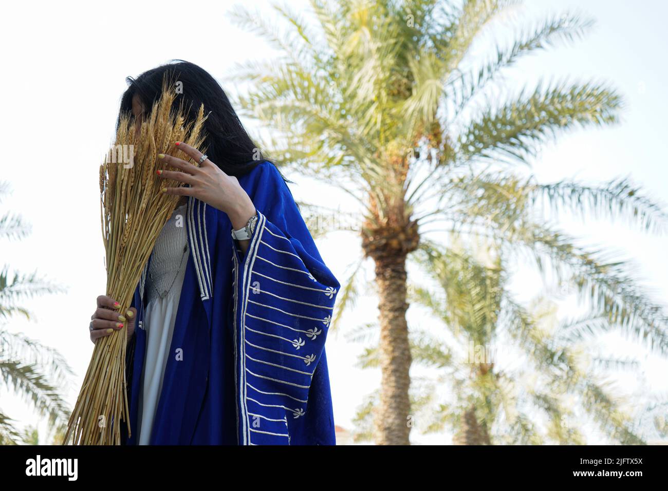 Donna che indossa Blue Abaya, Saudi Abaya con palme sfondo che tiene un burlap. Foto Stock