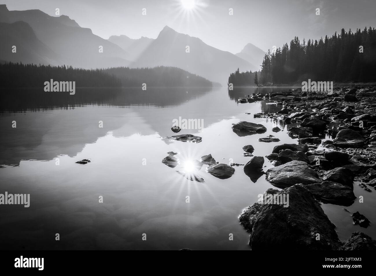 Lago ancora alpino che riflette il sole e le montagne circostanti e boschi, monocromatico, Jasper NP, Canada Foto Stock