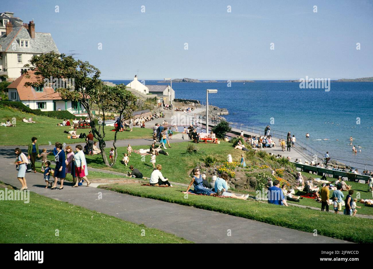 La gente si siede sull'erba vicino alla costa godendo il sole alla stazione balneare di Portrush, contea di Antrim, Irlanda del Nord, UK 1960s Foto Stock