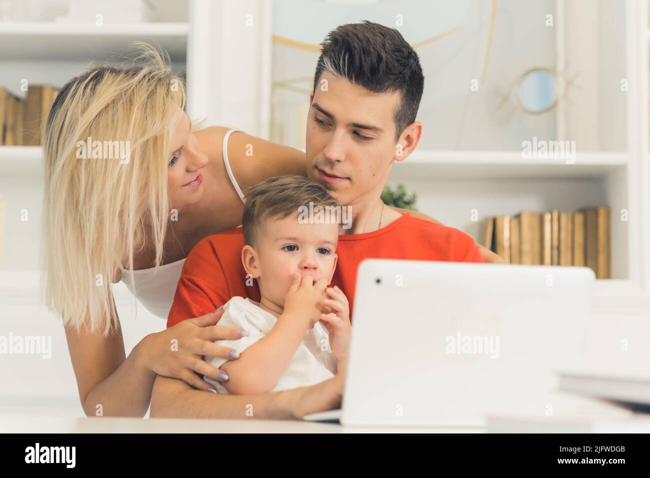 giovane coppia che guarda qualcosa nel portatile con il loro figlio piccolo, medio closeup concetto di famiglia indoor. Foto di alta qualità Foto Stock