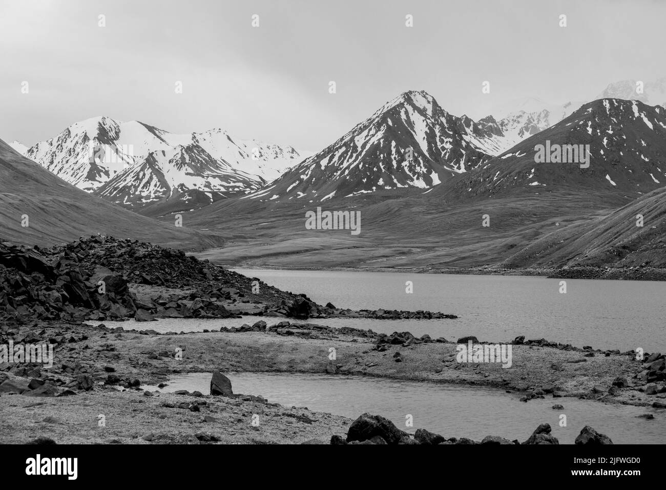 Colpo bianco e nero di un lago circondato da cime innevate in Kirghizistan. Foto Stock