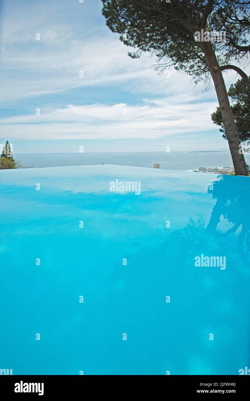 Una piscina a sfioro all'aperto con spazio per fotocopie. Angolo basso di una piscina vuota con acqua pulita e limpida circondata da alberi verdi e un cielo blu. Lusso Foto Stock