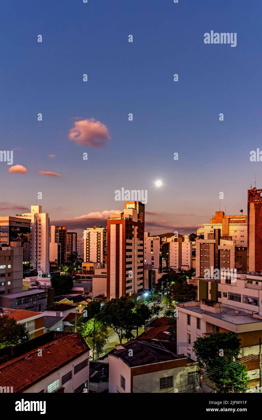 Distretto della città di Belo Horizonte a Minas Gerais con i suoi edifici illuminati dal tramonto e con la luna piena che sorge sullo sfondo Foto Stock