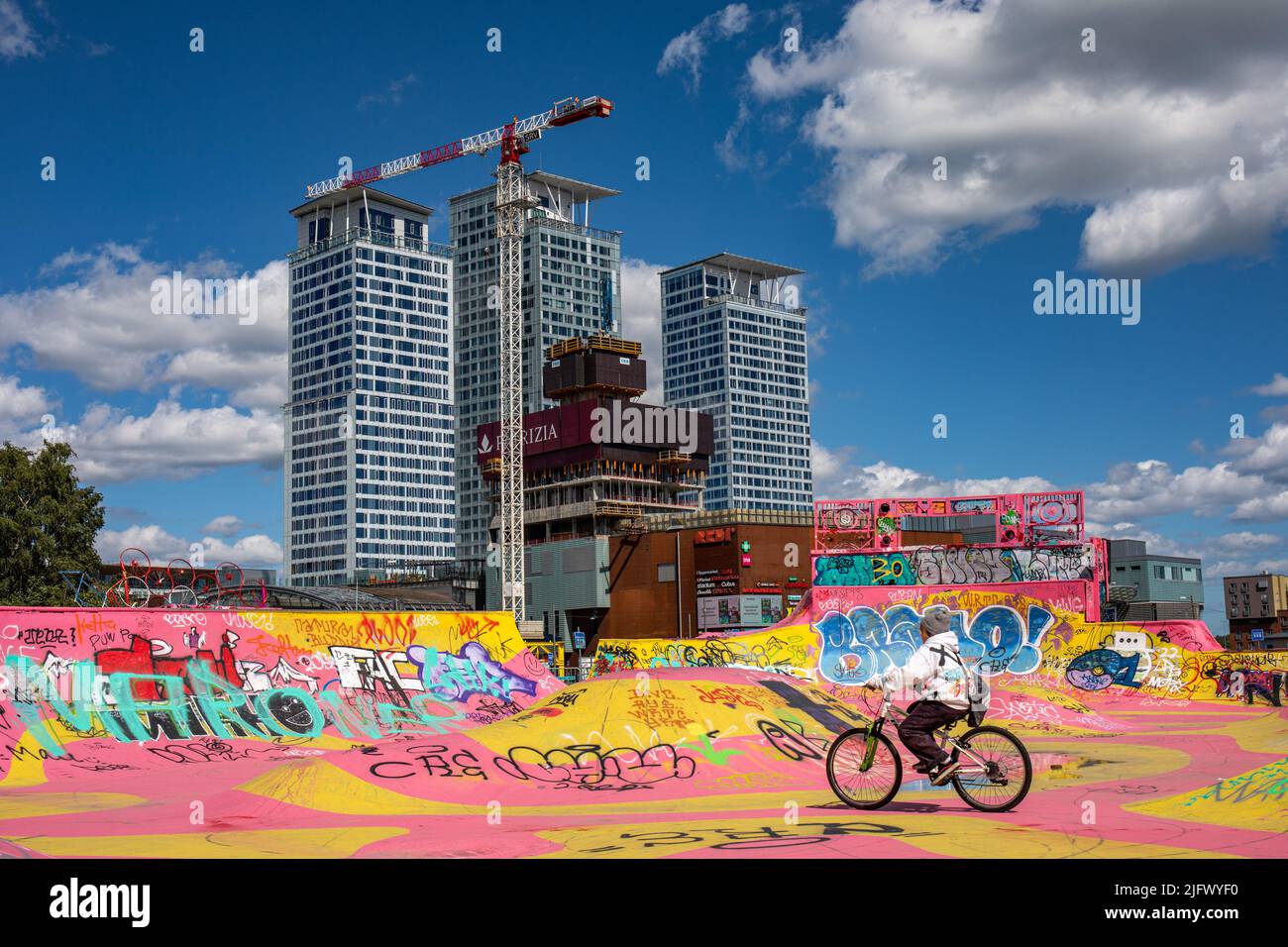 Bicicletta ragazzo, rosa e giallo Suvilahti DIY Skatepark e Kalasatama alti edifici a Helsinki, Finlandia Foto Stock