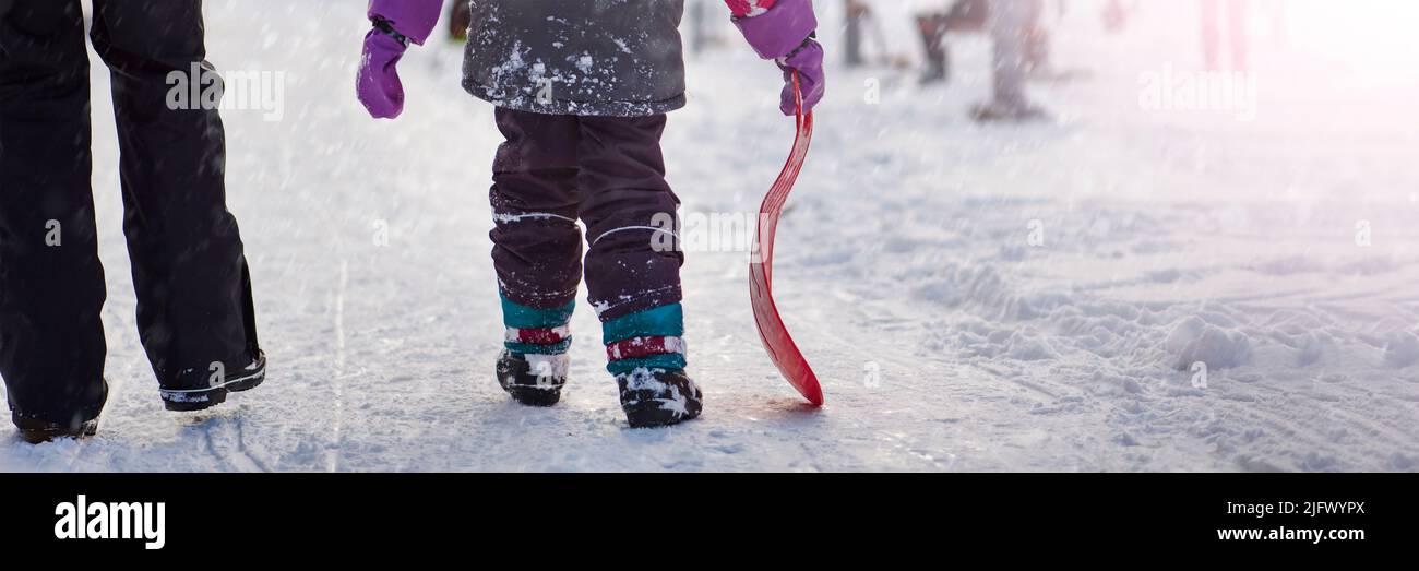 La ragazza sta tenendo una slitta rossa nelle sue mani per guidare la collina. Slittino. Attività per bambini e adolescenti. Animazione invernale e sport. Foto Stock