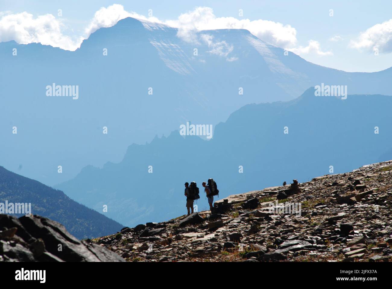 Scienziati USGS in silhouette contro uno sfondo di montagna... ritorno da un sito di studio dell'ecosistema alpino nel Glacier National Park, Montana, dove stanno ricercando e monitorando i potenziali impatti dei cambiamenti climatici sugli ecosistemi montani. Credito: G.Pederson, USGS. Foto Stock