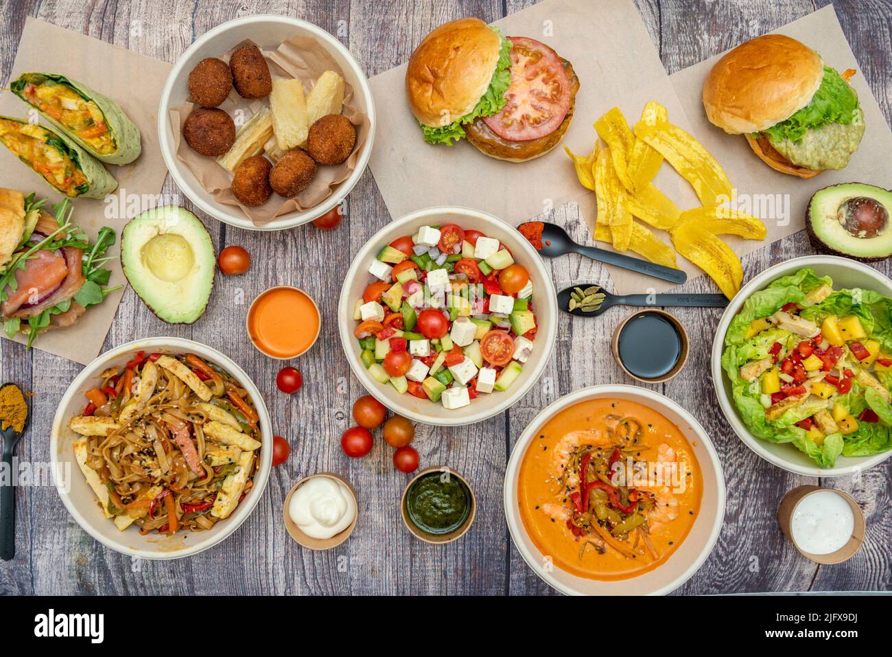 Set di piatti, insalate, cibo latino, hamburger, avocado e pomodori ciliegini su un tavolo marrone Foto Stock