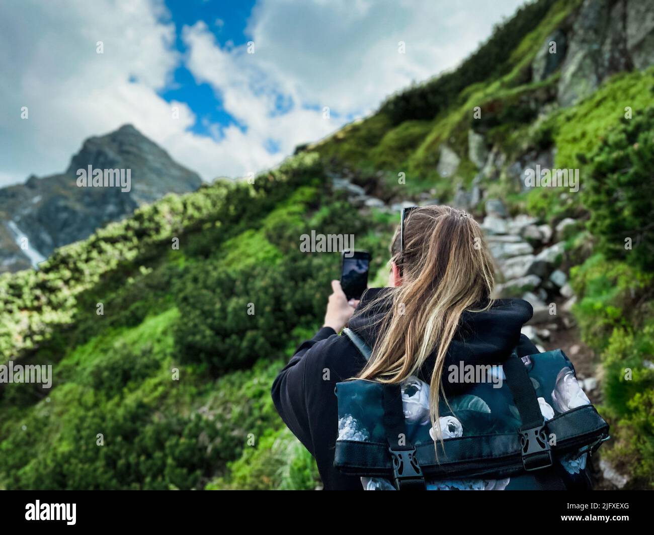 Giovane donna turistica con zaino che scatta foto al telefono in montagna Foto Stock
