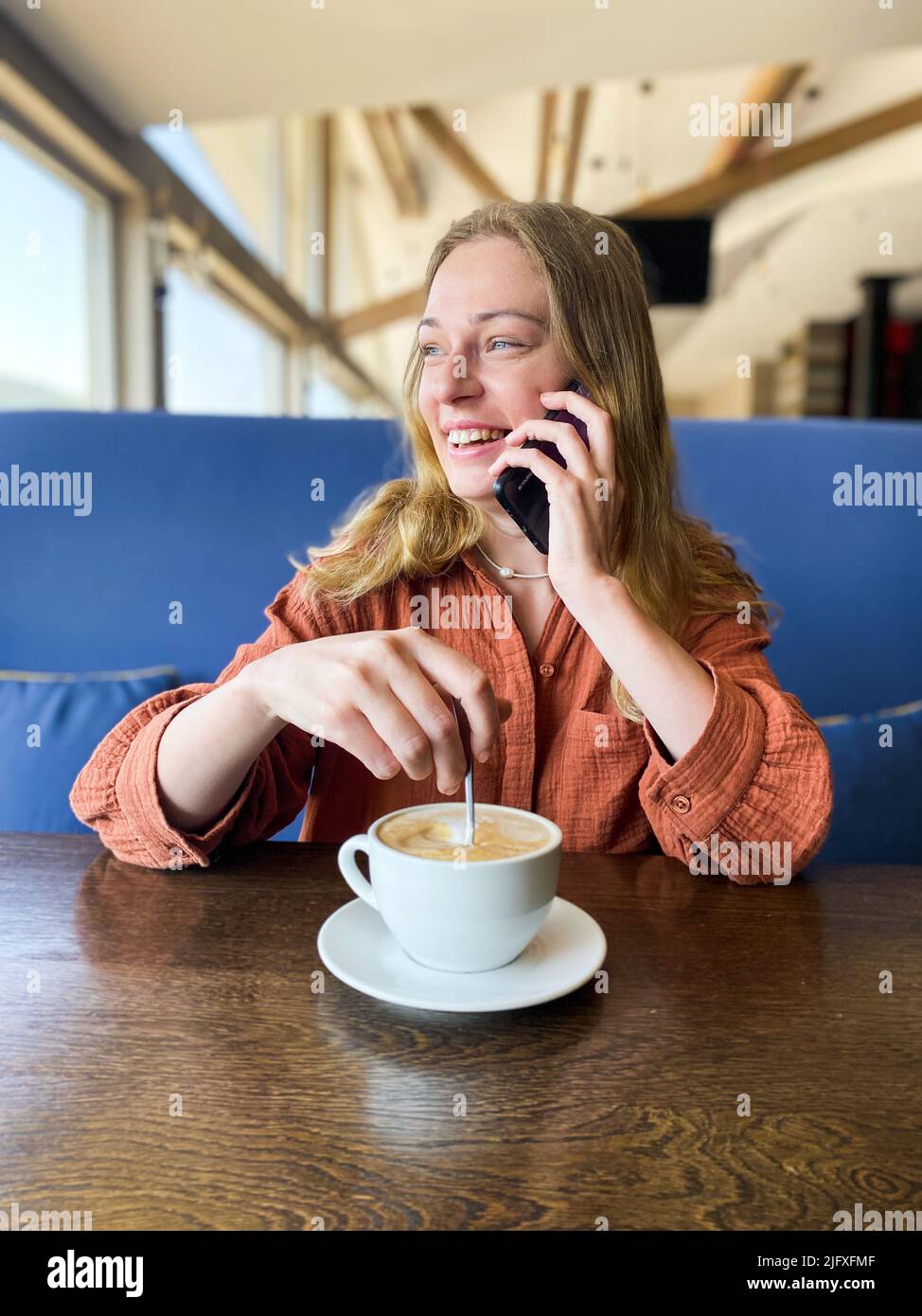 Una ragazza in un caffè beve caffè e parla al telefono. Foto Stock