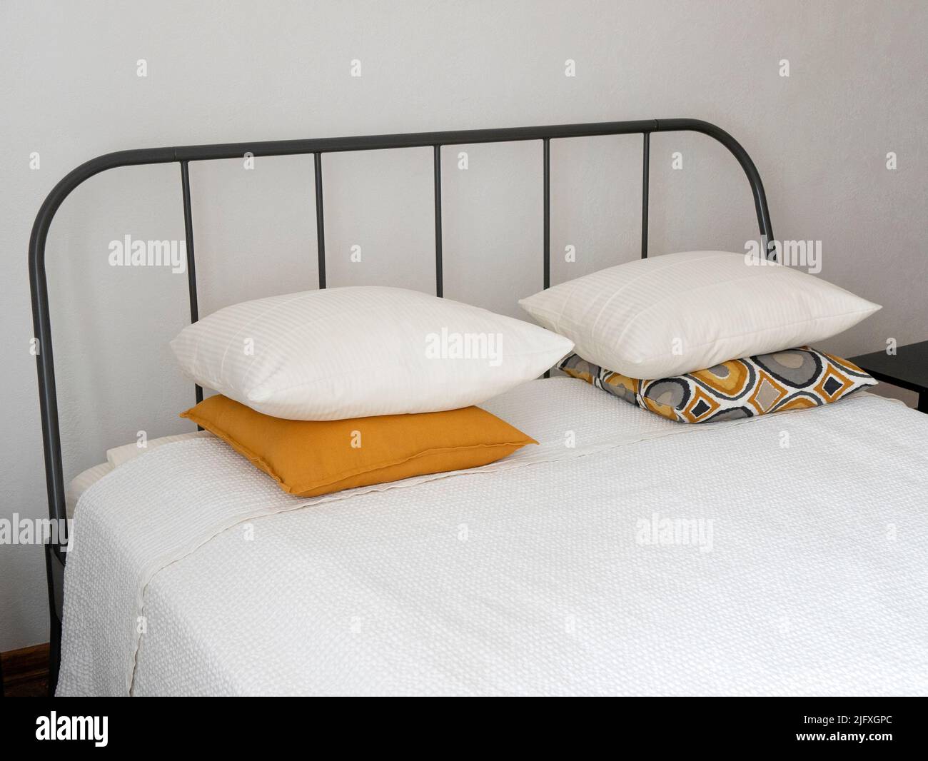 Letto con testiera in metallo, copriletto bianco neve e cuscini luminosi. Camera moderna e luminosa con letto in ferro da stiro Foto Stock