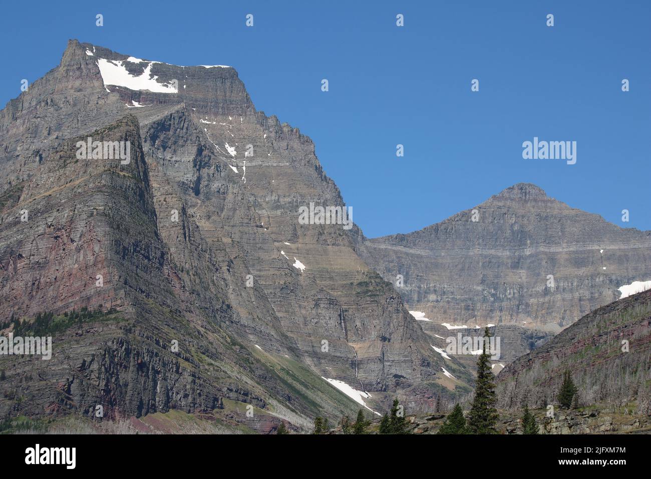 Vista est di rocce colorate a fasce di maestoso Going-to-the-Sun Mountain, Matahpi Peak, cascata e cascate, pini, Glacier National Park, MT, STATI UNITI Foto Stock