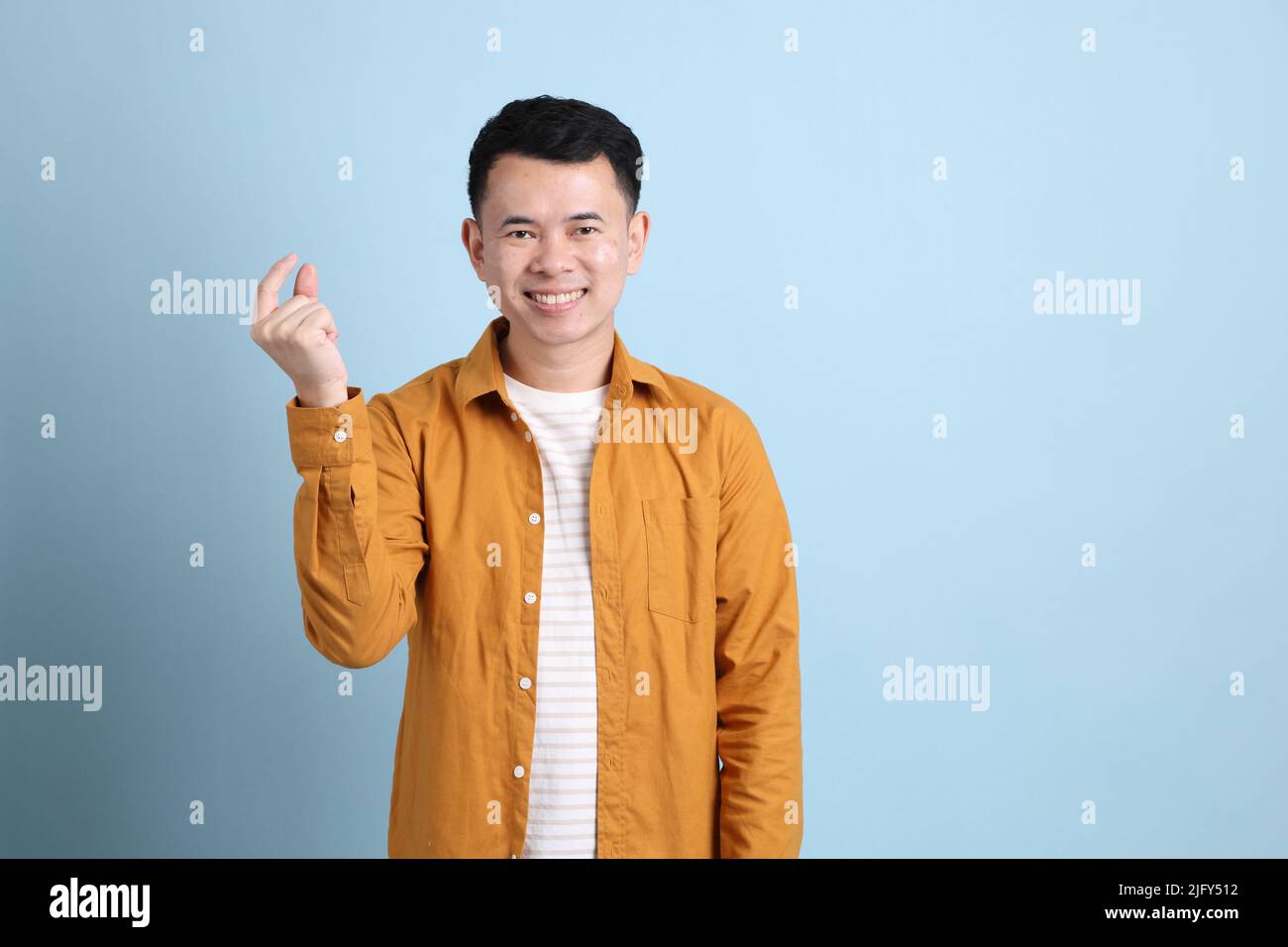 L'uomo asiatico LGBTQ con camicia gialla in piedi su sfondo blu. Foto Stock