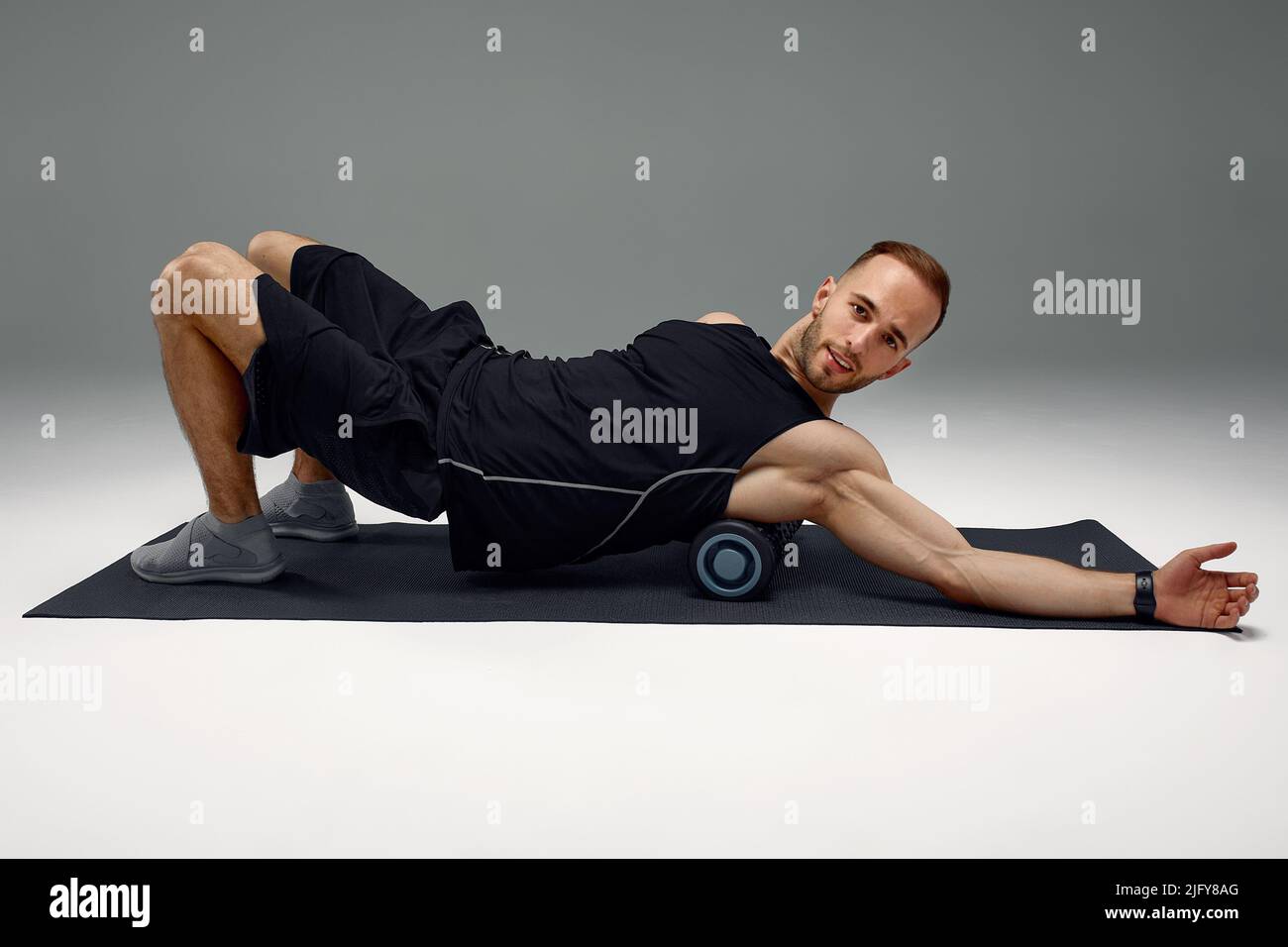 Athletic uomo usando un rullo in gomma spugna per alleviare muscoli doloranti dopo un allenamento. Foto Stock