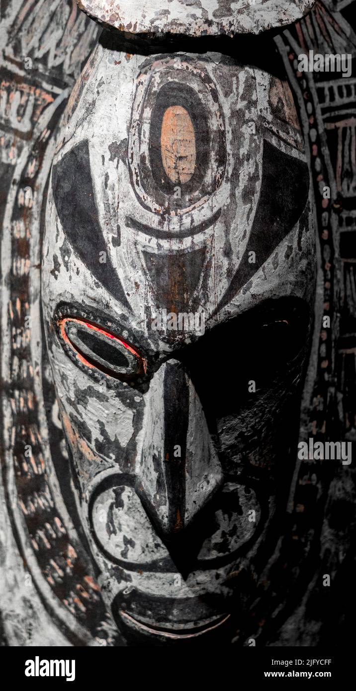 Una maschera di legno africano espressiva evidenzia la luce proveniente dal lato destro su sfondo scuro. Foto Stock