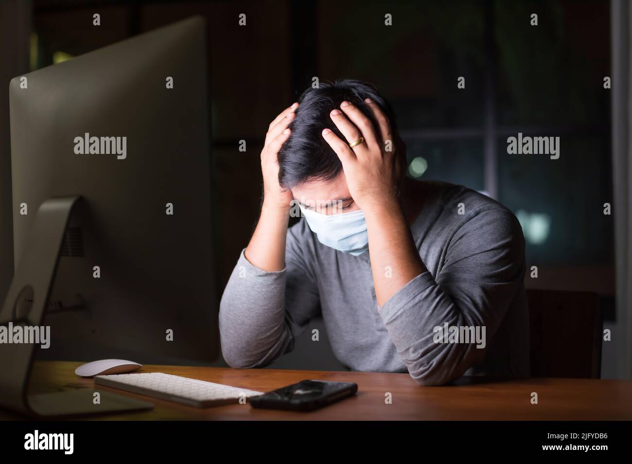 Uomo asiatico indossare maschera preventiva e lavorare da casa di notte in situazione di malattia di Corona Virus (COVID-19). Lavoro da casa e sano Foto Stock
