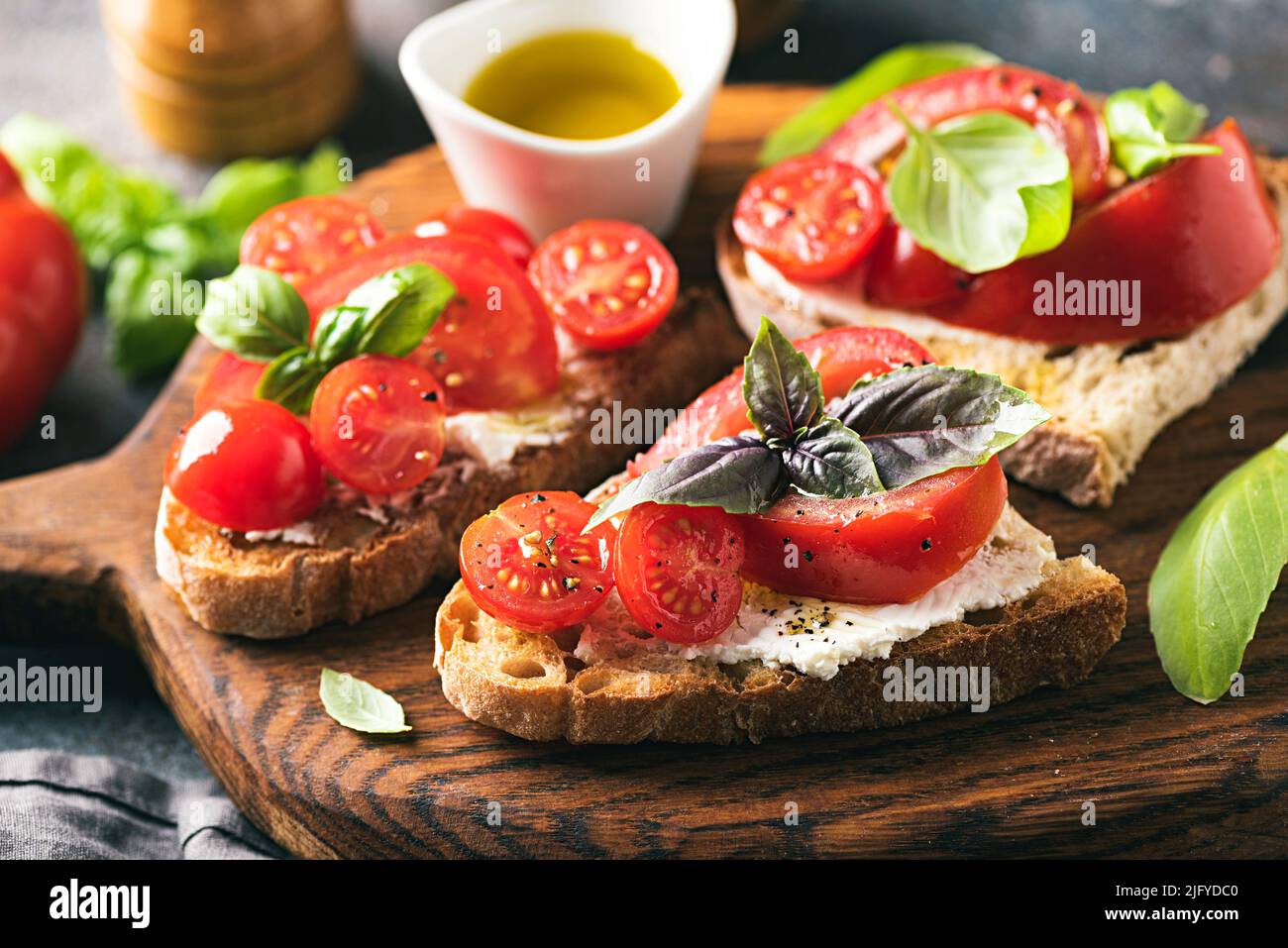 Bruschetta con pomodori, basilico e olio d'oliva su tavola di legno. Antipasto di cucina italiana Foto Stock