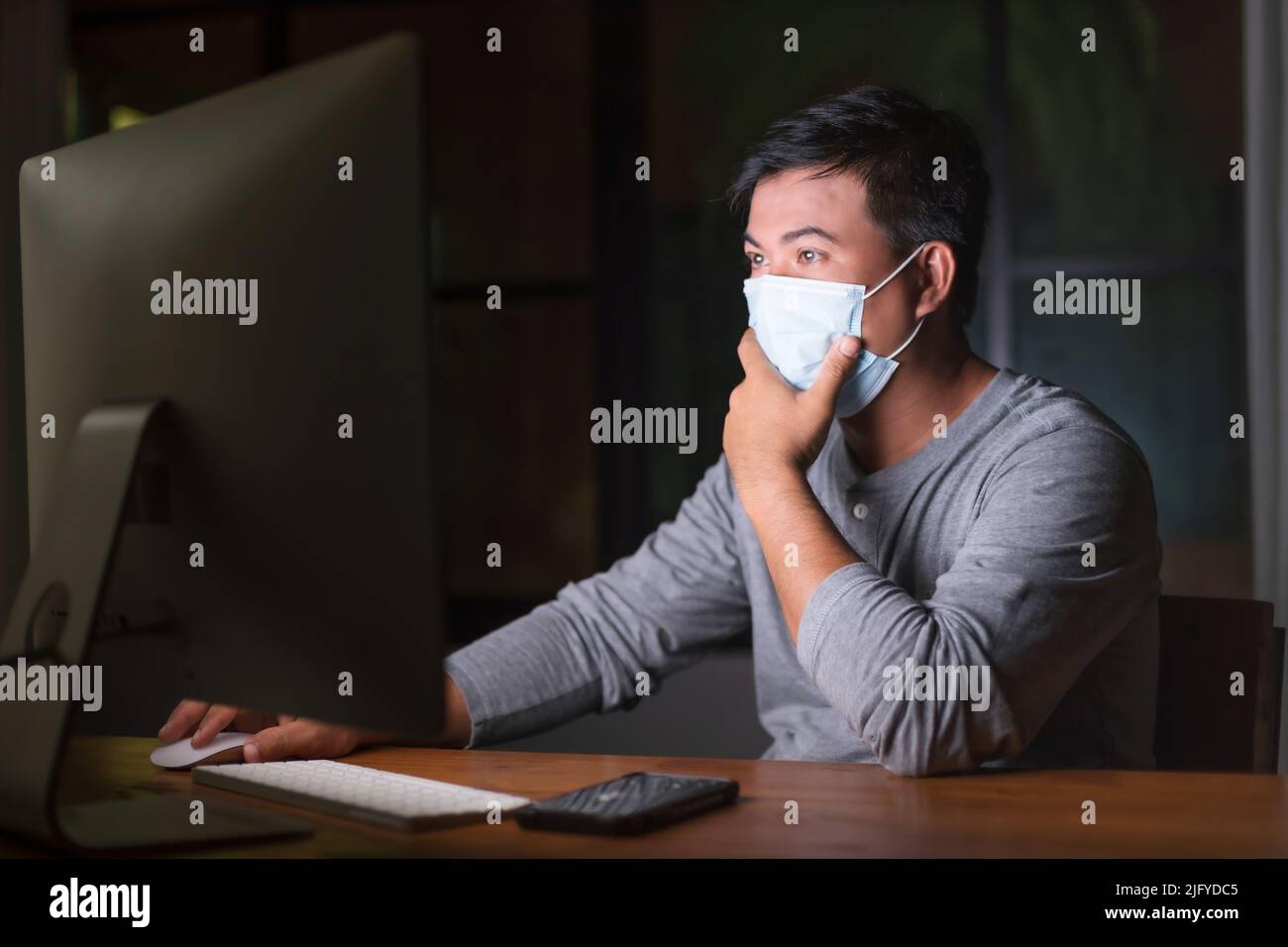 Uomo asiatico indossare maschera preventiva e lavorare da casa di notte in situazione di malattia di Corona Virus (COVID-19). Lavoro da casa e sano Foto Stock