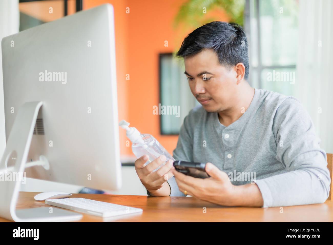 Uomo asiatico tenendo e guardando a mano igienizzatore gel bottiglia che ha ordinato di utilizzare a casa, il lavoro da casa e sano concetto Foto Stock