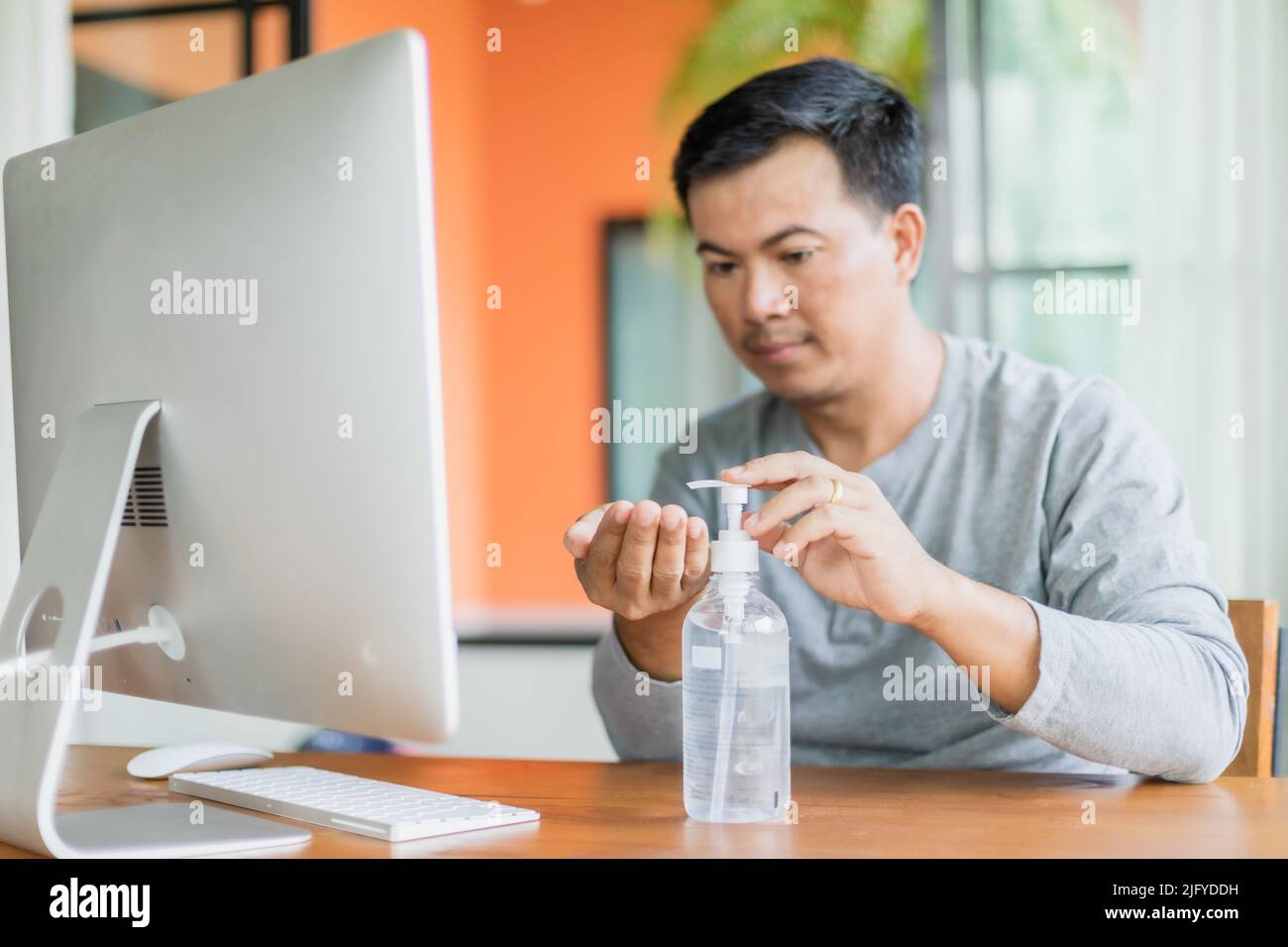 Uomo asiatico che usa il gel igienizzante per le mani per pulire la sua mano, lavorare da casa e sano concetto Foto Stock
