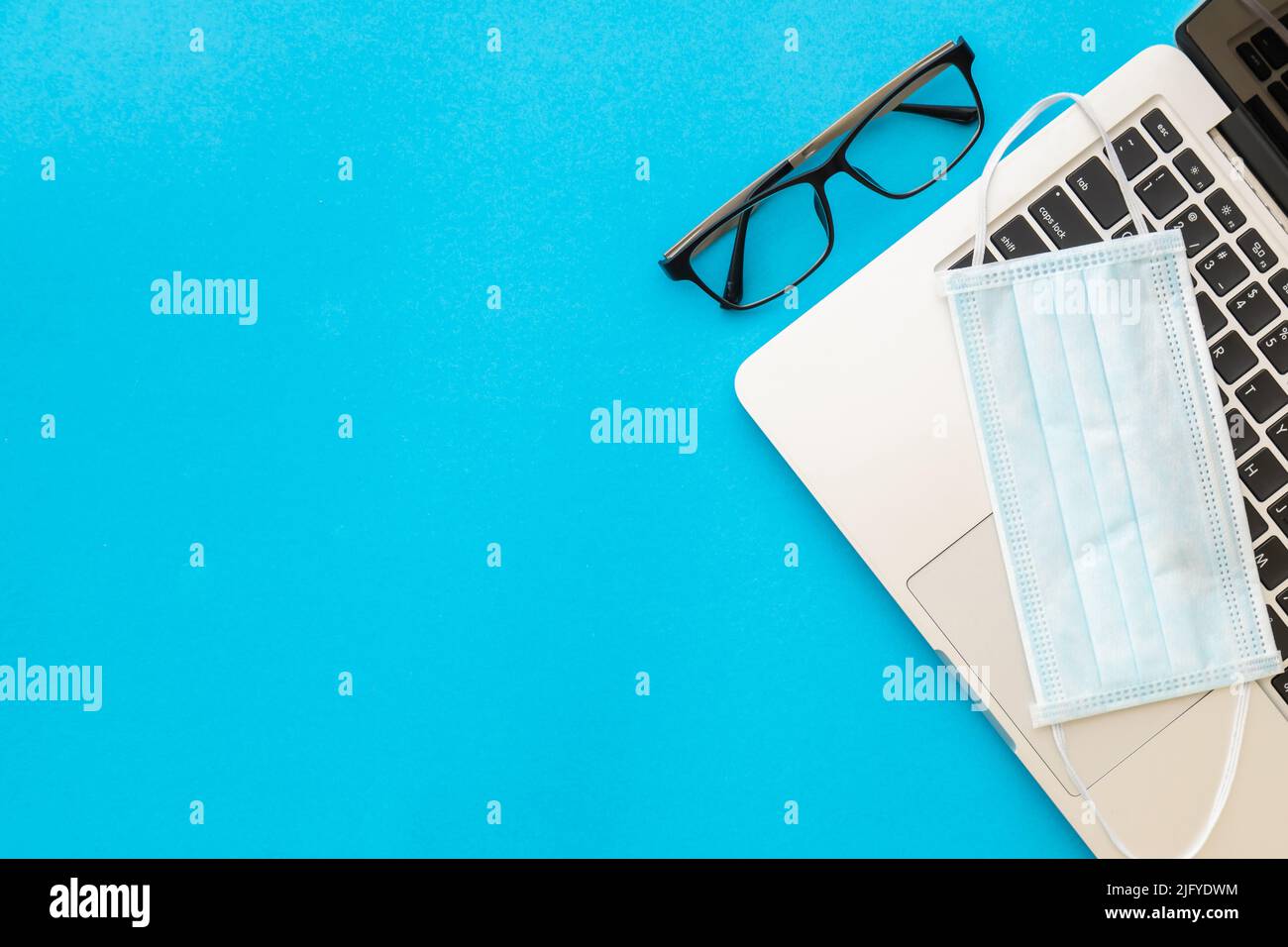 Vista dall'alto della nuova maschera preventiva sul laptop e degli occhiali su sfondo blu con spazio di copia per il testo o il design. Coronavirus (COVID-19) o Salute Foto Stock