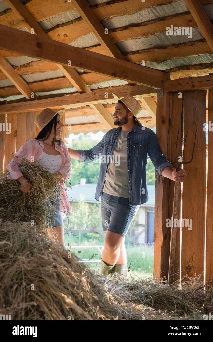 un uomo allegro che parla con la moglie accatastando hey in fienile mentre lavora in fattoria Foto Stock