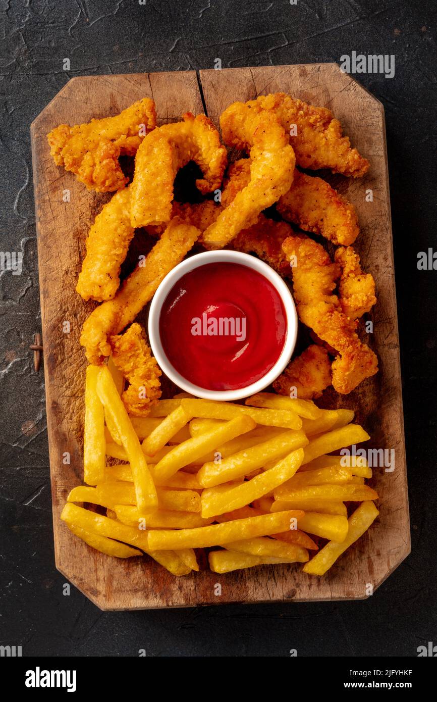 Polli, spicchi croccanti in pastella e fritti, con salsa barbecue e patate, su sfondo nero ardesia, top shot Foto Stock