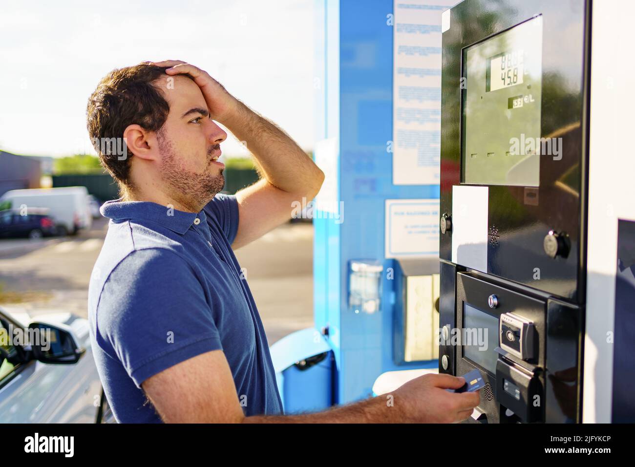 Giovane caucasico sorpreso dai prezzi elevati del carburante sul quadro di valutazione della stazione di servizio. Foto Stock