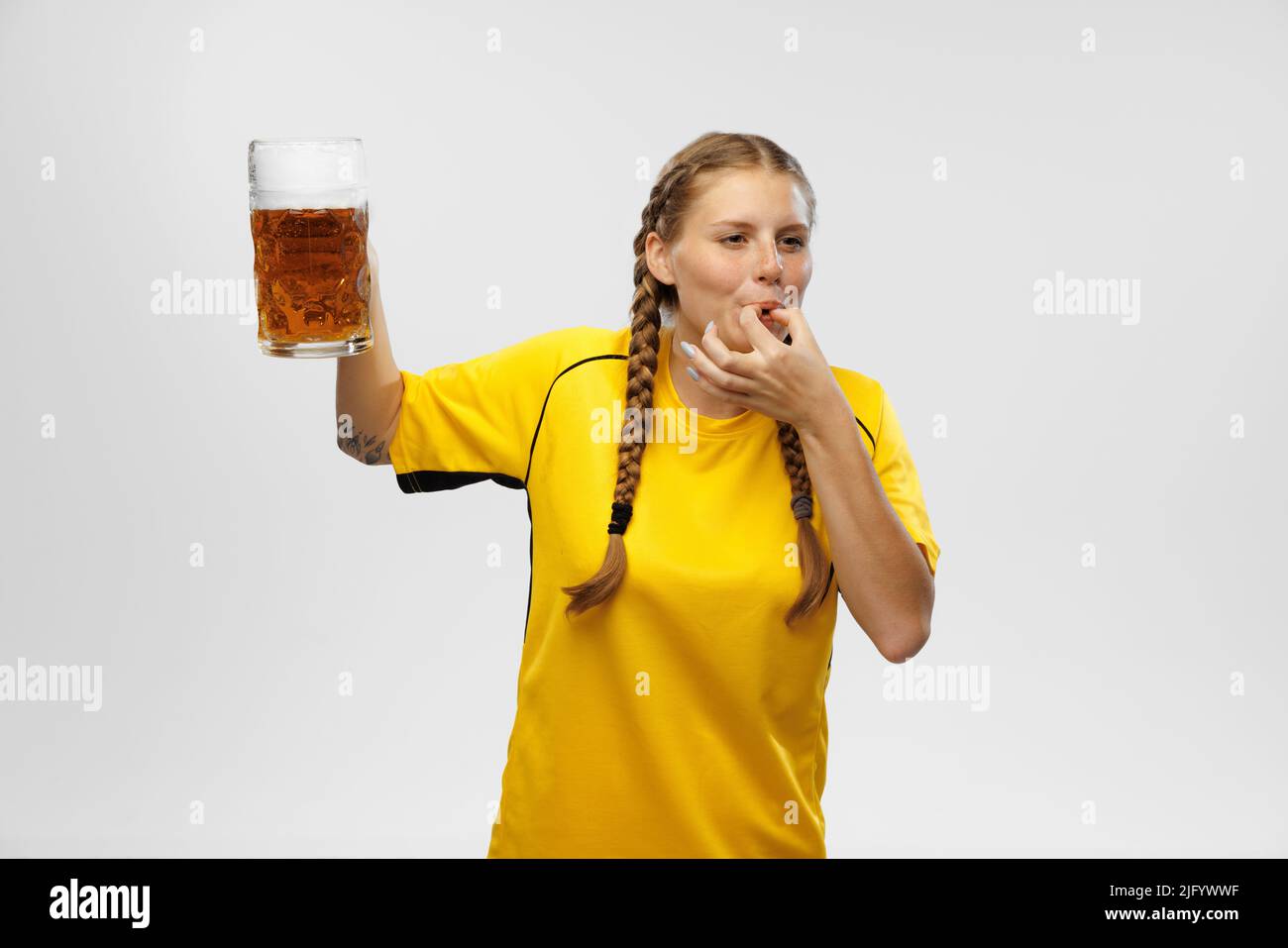 Giovane donna eccitata in divisa da calcio gialla con tazza di birra e supporta la squadra preferita. Appassionati di calcio, competizione, sport, concetto oktoberfest Foto Stock