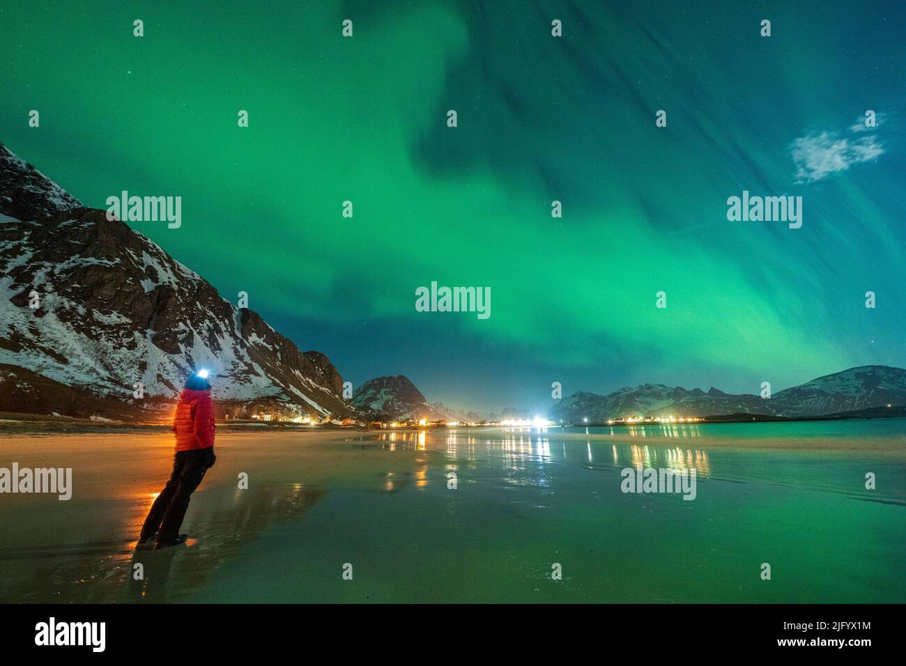 Escursionista con torcia di testa guardando l'aurora boreale (aurora boreale) in piedi sulla spiaggia di Ramberg, contea di Nordland, Isole Lofoten, Norvegia, Scandinavia Foto Stock