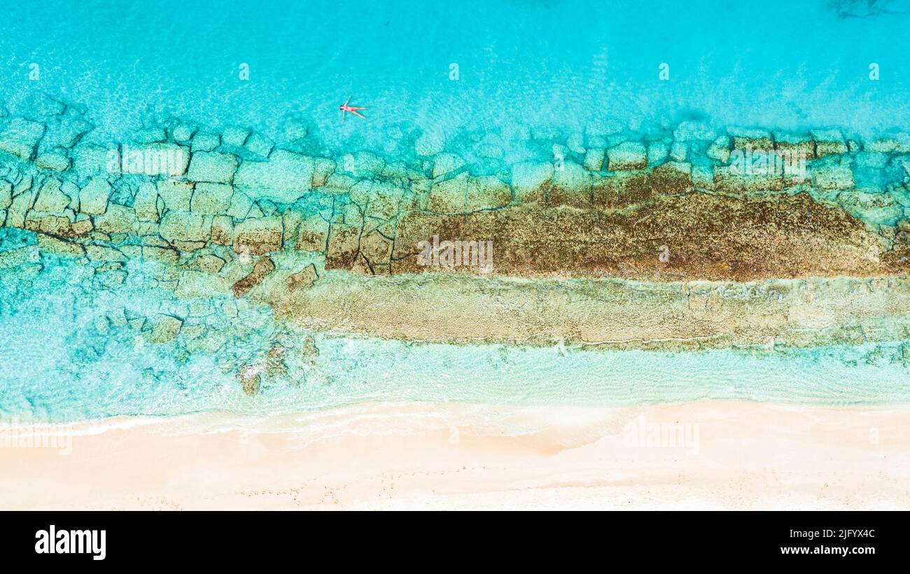 Veduta aerea della donna che galleggia sul mare cristallino tra la barriera corallina e la spiaggia di sabbia bianca, Antigua, Indie Occidentali, Caraibi, America Centrale Foto Stock