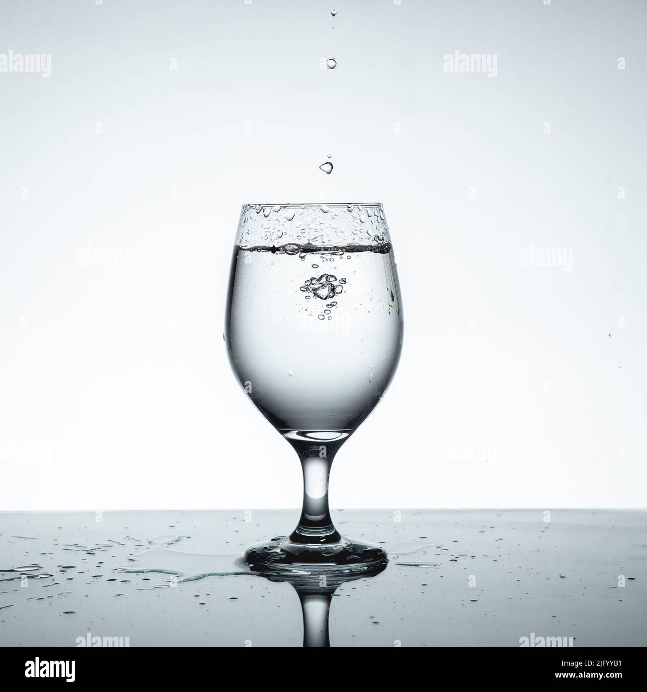 Bicchiere pieno d'acqua con gocce in caduta. Foto Stock