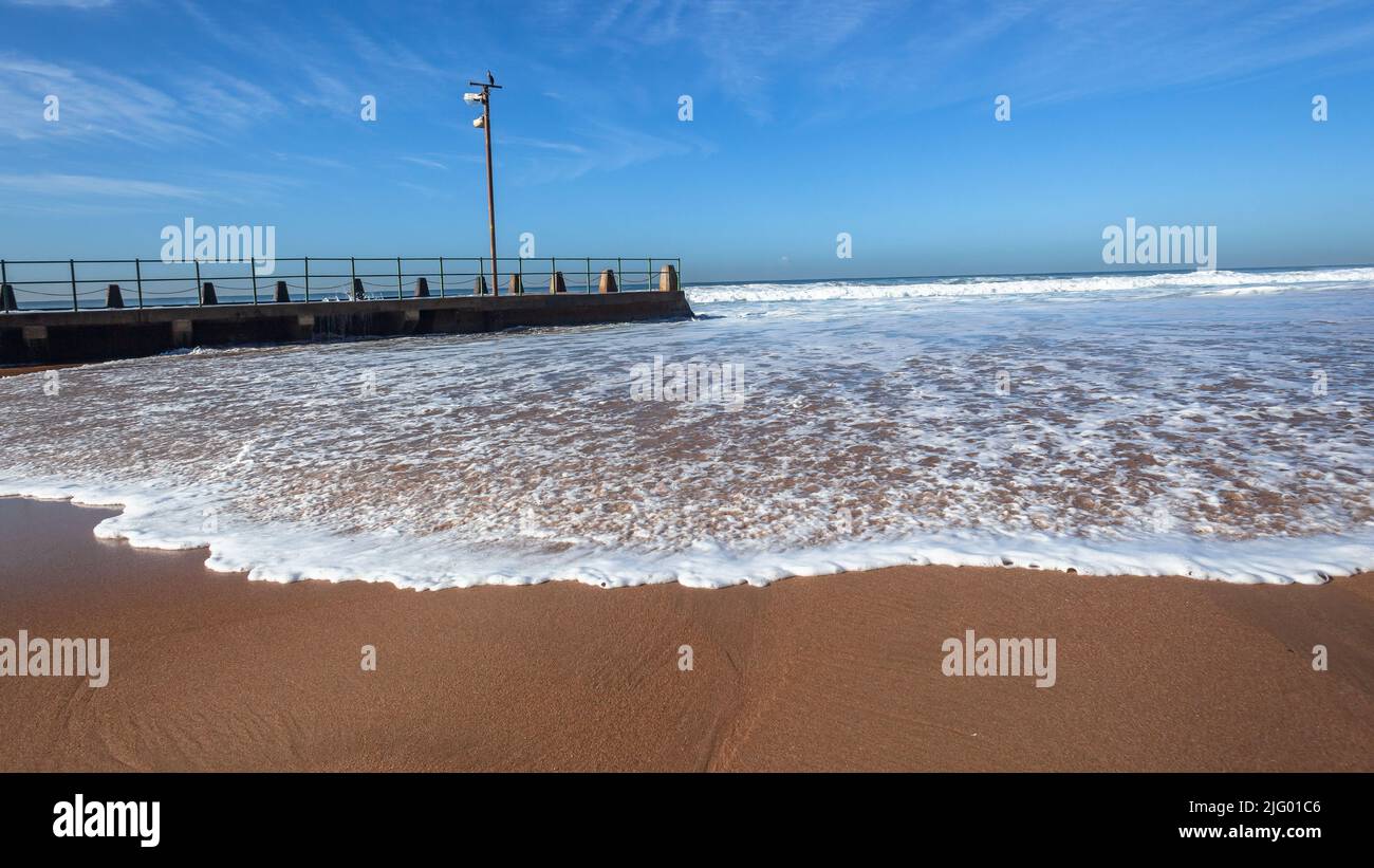 Spiaggia sabbia oceano mare onde acqua lavare intorno a calcestruzzo marea piscina con cielo del mattino. Foto Stock