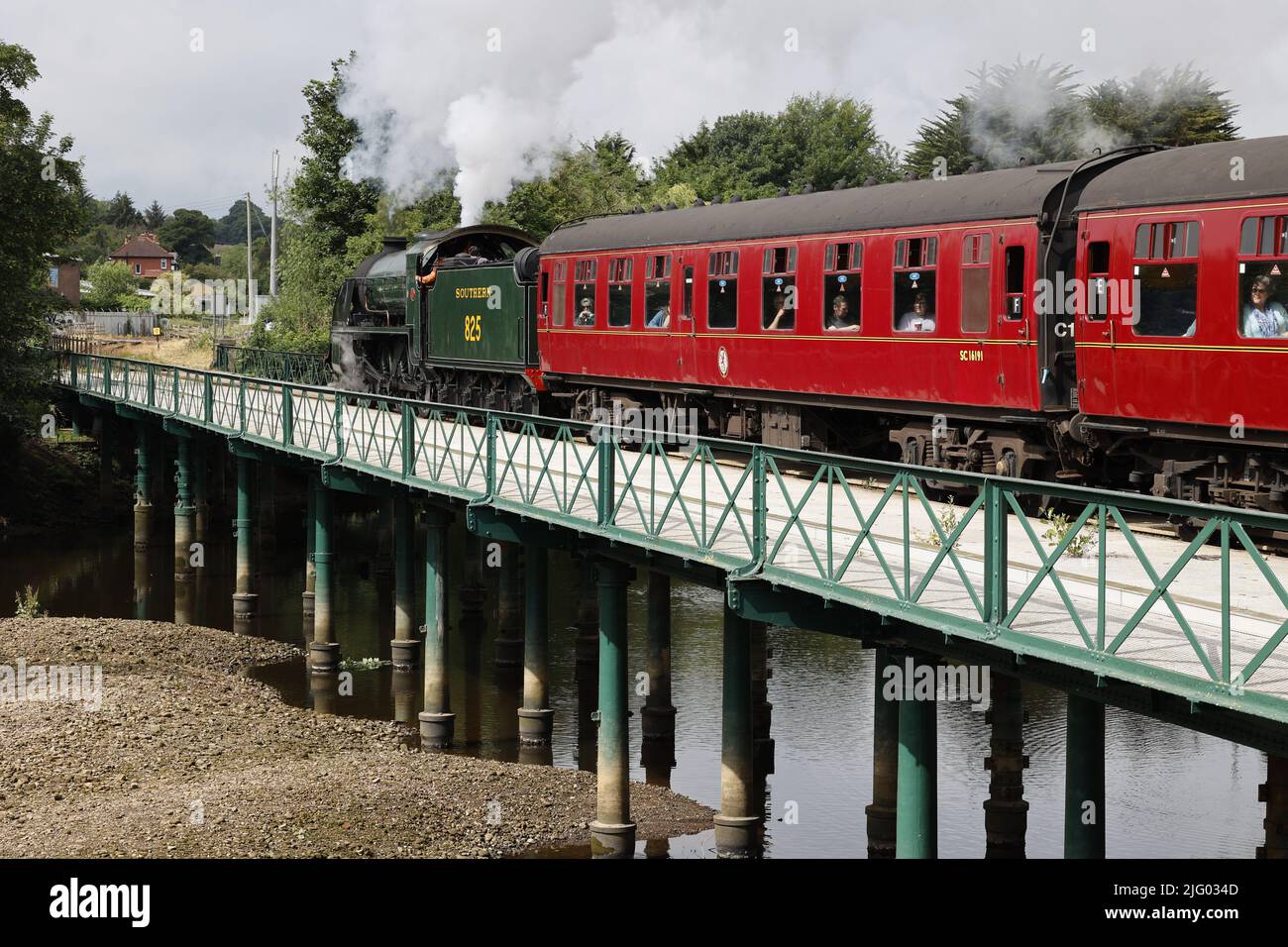 Treno a vapore (locomotiva classe SR S15) che traina carrozze passeggeri rosse attraverso il fiume Esk, North Yorkshire, Regno Unito Foto Stock